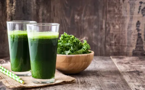 Dwa szklanki zielonego smoothie, miska jarmużu i słomki. Idealne na śniadanie zgodne z dietą sirtuinową.