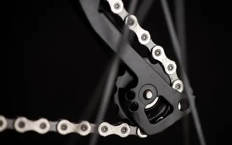 Jak dobrać łańcuch do roweru? Detal przerzutki tylnej z metalowym łańcuchem rowerowym na czarnym tle.