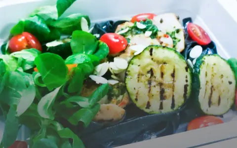 Kolorowy catering dietetyczny z grillowaną cukinią, pomidorkami i zielonymi liśćmi. Dowiedz się, jak podgrzewać catering dietetyczny, by zachować świeżość.