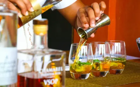 Ein Barkeeper gießt bernsteinfarbenen Rum in Gläser mit Eis und Minze. Die Frage "ab wann brennt Schnaps" wird hier durch das Servieren von edlem Rum beantwortet.
