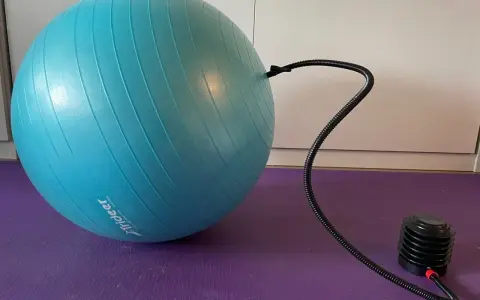 Niebieska piłka fitness podłączona do pompki na fioletowej macie.
