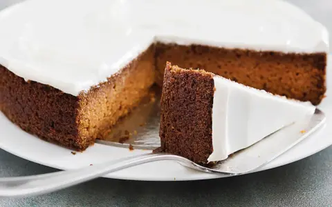 Una fetta di torta di carote e yogurt, soffice e ricoperta di glassa bianca, pronta per essere gustata.