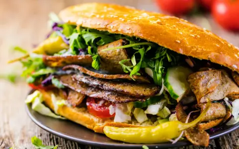 Duży kebab w bułce z mięsem, warzywami i sosem na drewnianym tle.