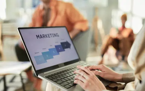 Osoba pracuje na laptopie z prezentacją "MARKETING". Widoczne etapy: Research, Analysis, Sales. Idealne do studiów zarządzanie i marketing.