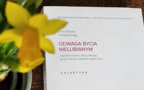 Żółty narcyz obok książki "Odwaga bycia nielubianym". Odkryj sztukę bycia sobą i wolności.