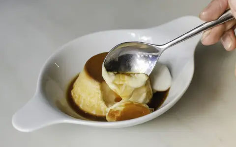 Una cuchara saca un trozo cremoso de flan de cuajada, bañado en caramelo líquido.