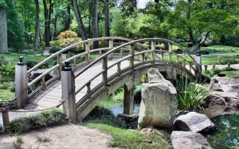Eine hölzerne Bogenbrücke führt durch den grünen Herford Park. Ein kleiner Bach plätschert unter der Brücke hindurch.