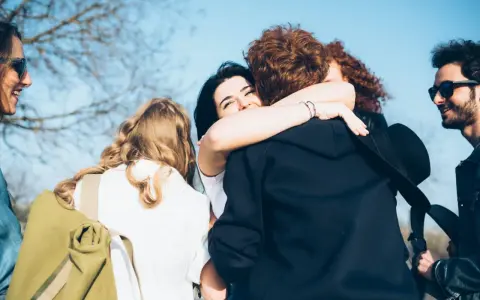 Grupa przyjaciół się przytula. W tle błękitne niebo. Idealny moment na fajne cytaty na podziękowanie.