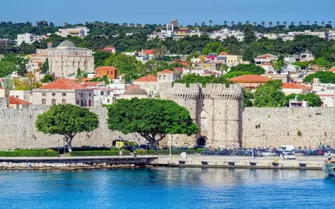 Widok na zabytkowe mury obronne i zabudowania wyspy Rodos, z błękitnym morzem w tle.