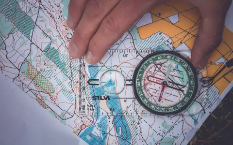 En hand håller en kompass över en karta, vilket visar hur fungerar en kompass för orientering.