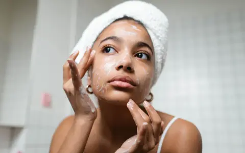 Rutina de limpieza facial: mujer con toalla en la cabeza aplica espuma en su rostro, un paso esencial para como cuidar mi piel.