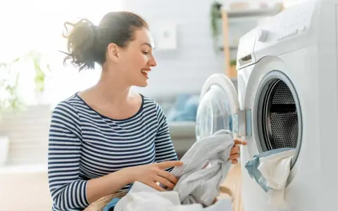 Donna sorridente carica la lavatrice, mostrando il funzionamento di un elettrodomestico moderno per il bucato.