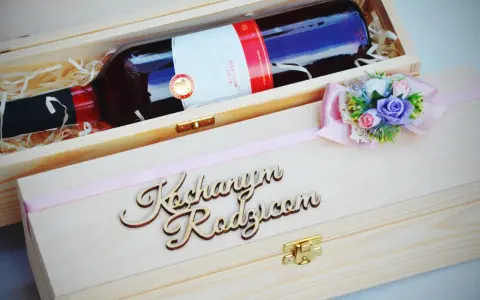 Elegancka skrzynka na wino dla chrzestnych z napisem "Kochanym Rodzicom" i ozdobną kokardką z kwiatami.
