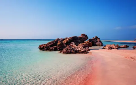 En rosa strand på Kreta med turkost vatten och klippor. En dröm för alla som älskar en kreta rosa strand.