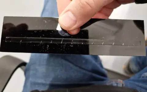 A hand holds a black acrylic strip with a precisely cut slot, demonstrating how to laser cut acrylic at home.