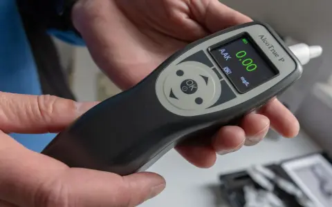 Hände halten ein Alkoholtestgerät, das 0.00 mg/L anzeigt. So vermeidet man eine Strafe wegen Alkohol am Steuer.