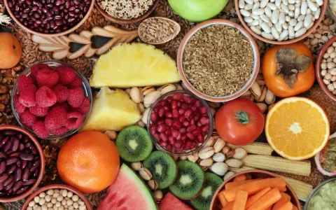 Vielfalt an ballaststoffreichen Lebensmitteln: Bohnen, Quinoa, Beeren, Obst, Gemüse und Nüsse für eine gesunde Ernährung.