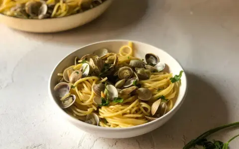Un invitante piatto di spaghetti alle vongole, con pasta dorata e molluschi freschi, guarnito con prezzemolo.
