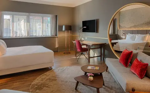 Modern hotel room with a bed, sofa, desk, and large round mirror reflecting the room.