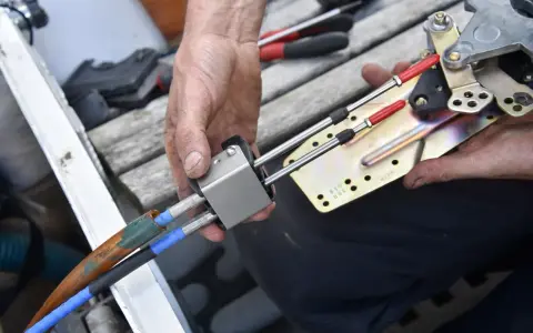 Main d'un mécanicien démontant le boîtier de commande d'un bateau, révélant les câbles et le mécanisme.