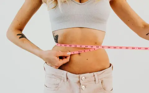 Kobieta mierzy talię centymetrem. Efekty diety 1400 kcal są widoczne.
