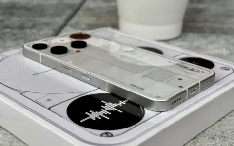 Przezroczysty telefon survivalowy z minimalistycznym designem, leżący na białym pudełku z grafiką.