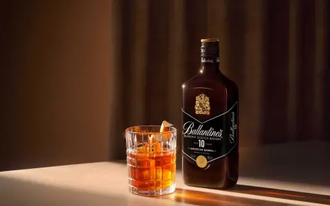 Elegancki drink Rob Roy z whisky Ballantine's 10 Year Old, podany w szkle z lodem i skórką pomarańczy.