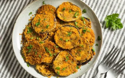Plato de berenjenas rebozadas, doradas y crujientes, espolvoreadas con perejil fresco.