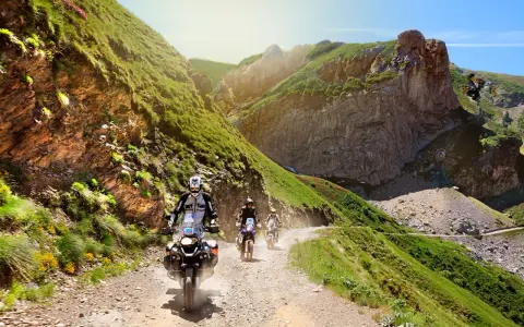 Un gruppo di motociclisti affronta un emozionante giro in moto in Liguria, su una strada sterrata tra montagne verdi e rocce imponenti.