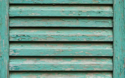 Persiane in legno fai da te con vernice verde acqua scrostata, che rivela il legno grezzo sottostante.