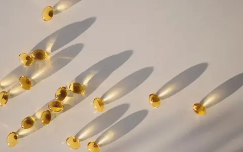 Gula kapslar med d-vitamin och magnesium sprids ut på en ljus yta, med långa skuggor som skapas av solljuset.