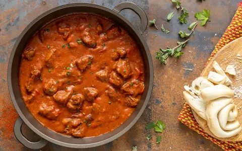 Un saporito gulash di manzo in una padella, accompagnato da pane fresco e erbe aromatiche.