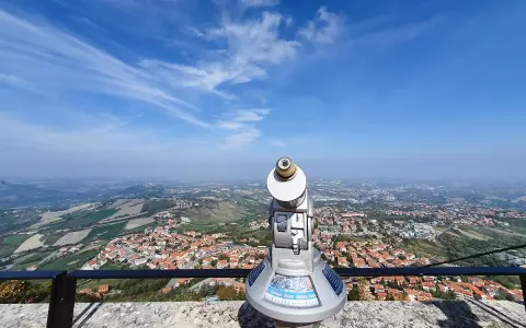 Telescopio con vista panoramica su cosa vedere a San Marino. Il paesaggio collinare e la città si estendono sotto un cielo azzurro con nuvole sottili.