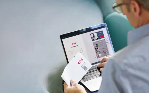 Mężczyzna loguje się do portalu eOS fundusz inwestycyjny. Na ekranie laptopa widnieje formularz logowania i informacje o inwestycjach.