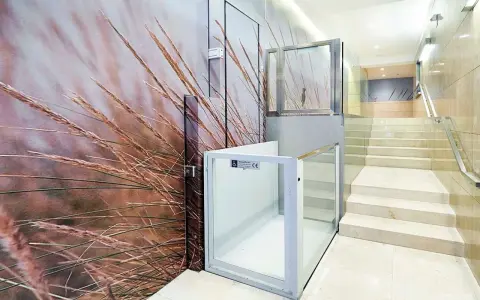 Un portal de vecinos moderno con un mural de hierbas secas y una plataforma elevadora de cristal.