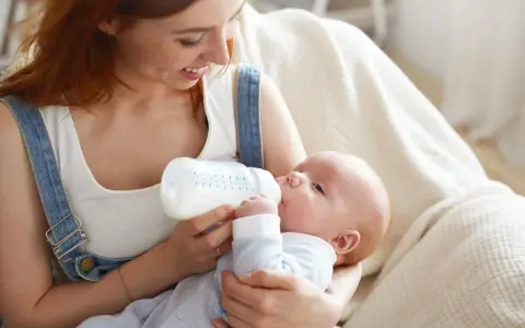 Uśmiechnięta mama karmi piersią swoje dziecko z butelki, szukając najlepszych butelek dla noworodka.