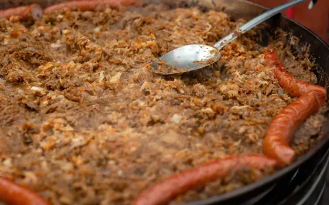 Wielki gar bigosu z kiełbasą, gotowy do wekowania w piekarniku. Łyżka zanurzona w aromatycznym daniu.