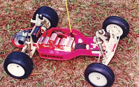 Ein ferngesteuertes Auto von Team Associated mit Batterien und Reifen auf Gras.