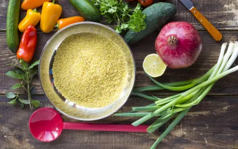 Schüssel mit Bulgur, einer tollen Quelle für **bulgur protein**, umgeben von frischem Gemüse wie Paprika, Gurken, Granatapfel und Frühlingszwiebeln.