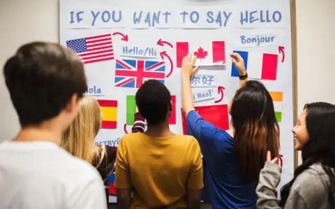 Uczniowie przy tablicy z flagami i napisami: "IF YOU WANT TO SAY HELLO". Rozwiązują zadanie, które może zawierać 10 pytań po angielsku.