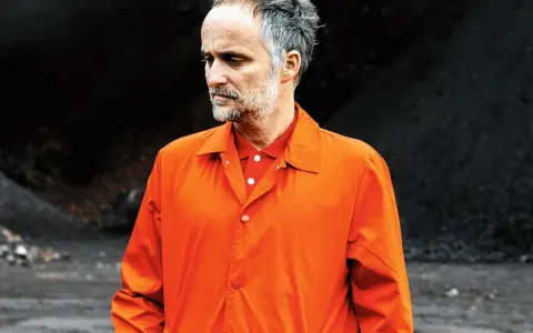 Artur Rojek w pomarańczowej kurtce, jakby zastanawiał się nad nowymi utworami.