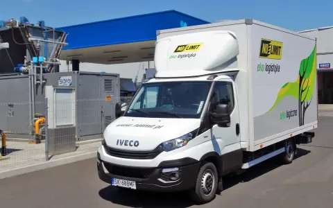 Biała ciężarówka Iveco zasilana gazem CNG, z logo "NO LIMIT eko logistyka", zaparkowana przy stacji paliw.