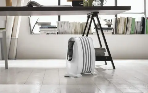 Un radiatore ad olio bianco, sotto una scrivania, mostra come funziona per riscaldare l'ambiente.