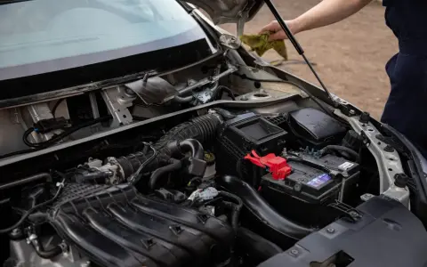 Silnik samochodu z widocznym akumulatorem i elementami układu dolotowego. Czy to zepsuty alternator czy akumulator?