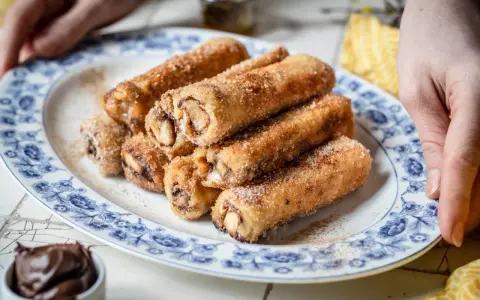 Nutella French Toast Rolls, goldbraun gebacken und mit Zimt-Zucker bestreut, auf einem Teller mit blauem Blumenmuster.