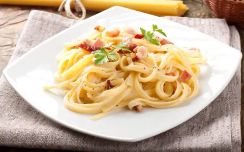 Pyszny makaron carbonara z boczkiem i natką pietruszki na białym talerzu.