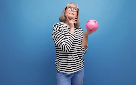 Mujer pensativa con hucha rosa, considerando los tipos de planes de pensiones para su futuro.