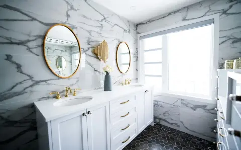 A modern bathroom vanity installation featuring white cabinets, marble walls, gold accents, and dual sinks.