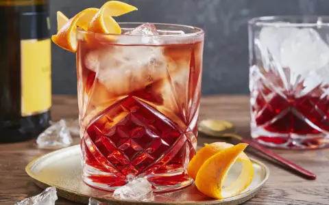 Ein erfrischender Negroni Sbagliato mit Eis und Orangenzeste, serviert auf einem goldenen Teller.