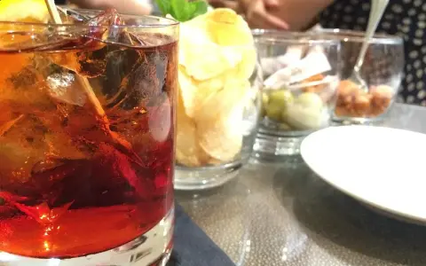Orzeźwiający drink z lodem i cytryną, obok chipsy i oliwki. Idealne połączenie, by dowiedzieć się, **sambuca z czym pić**.